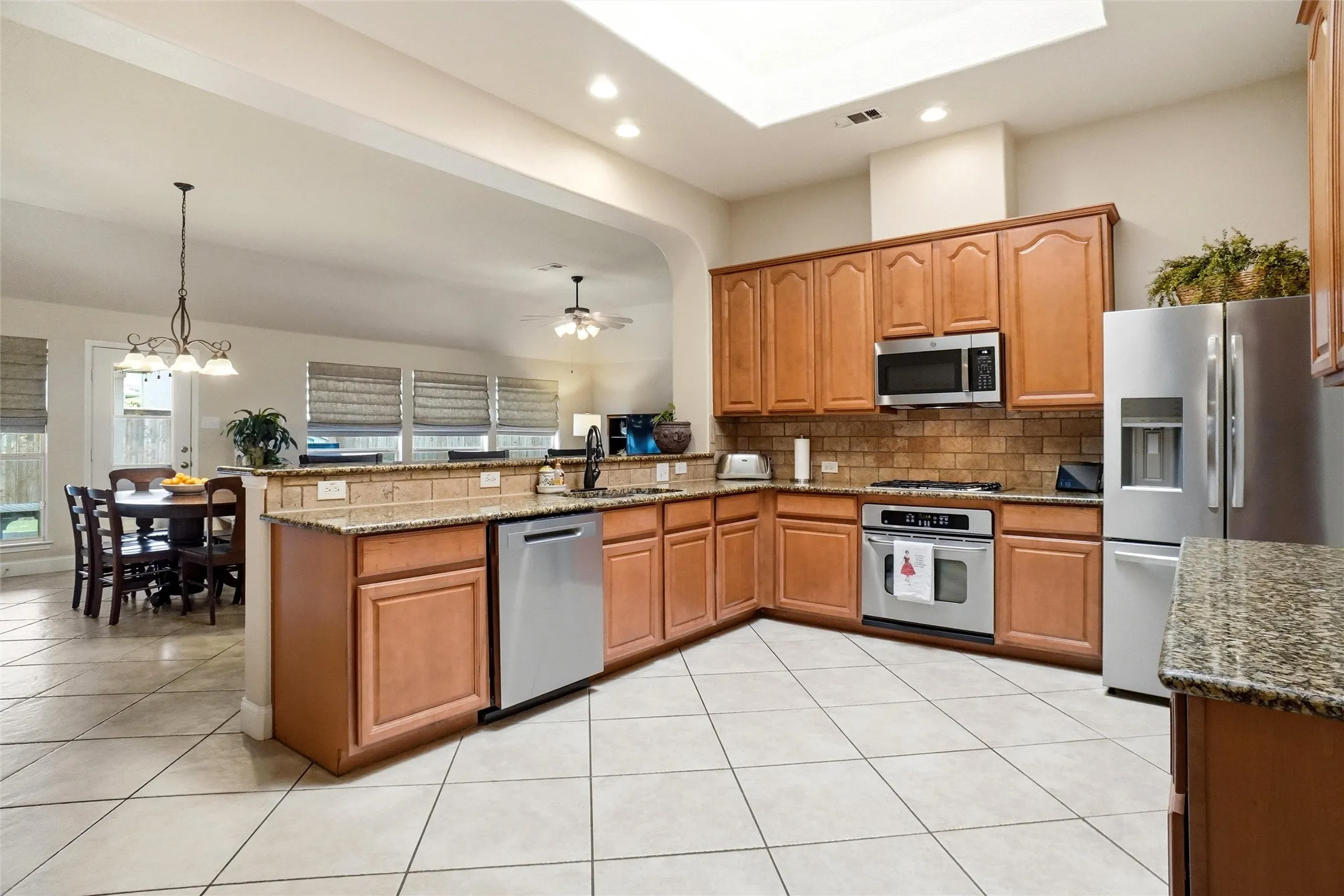 Kitchen featuring light wood cabinetry, stone countertops, stainless steel appliances, and a tiled backsplash