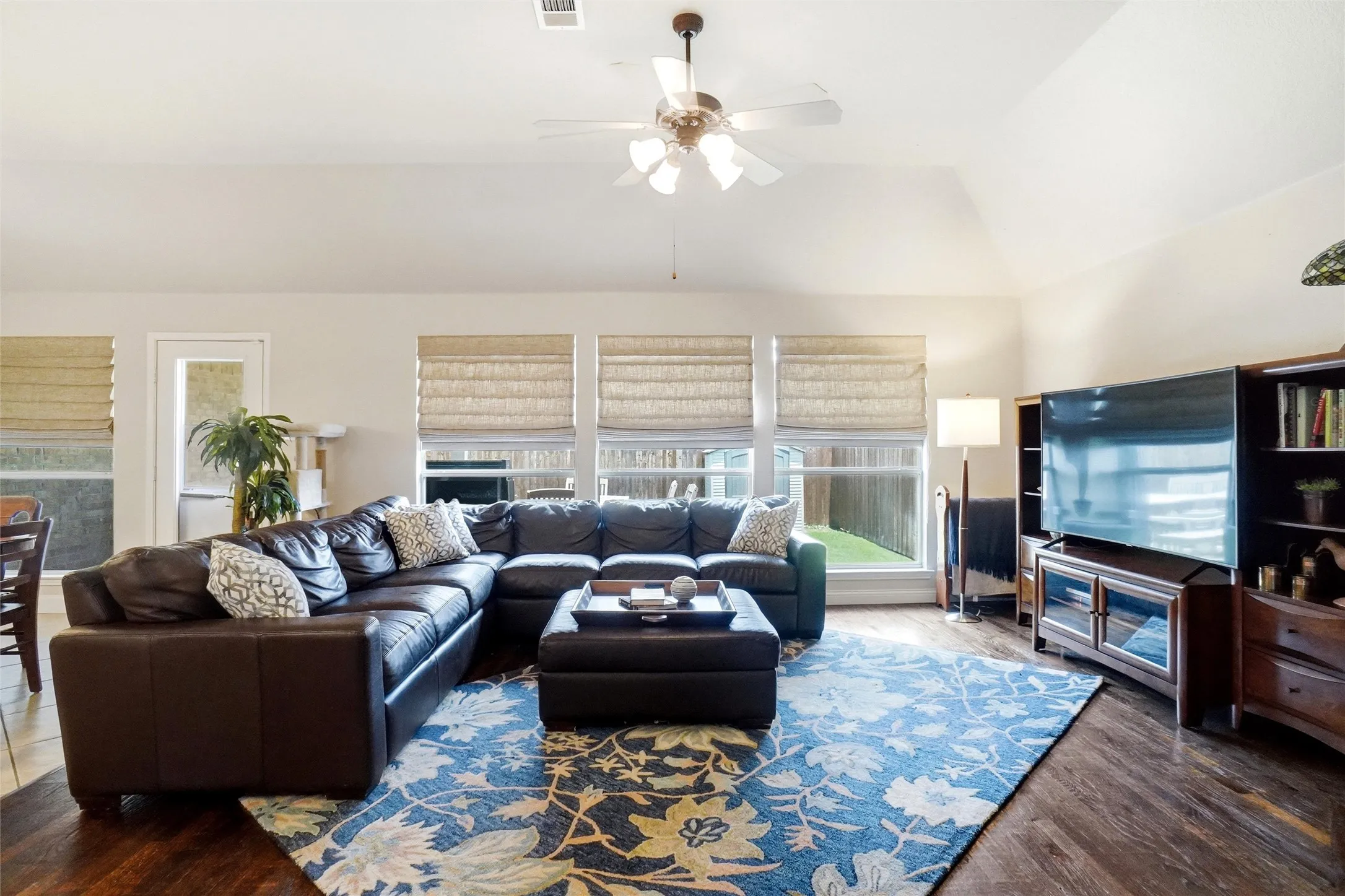 Spacious living area featuring wood-finish flooring, vaulted ceilings, and a ceiling fan