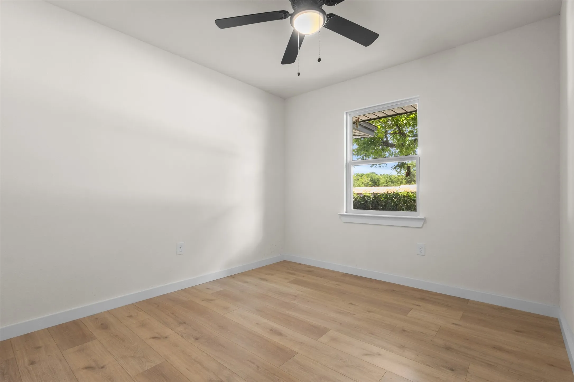 Room featuring a ceiling fan with integrated lighting, a window with exterior views, wood-finish flooring, and white baseboards