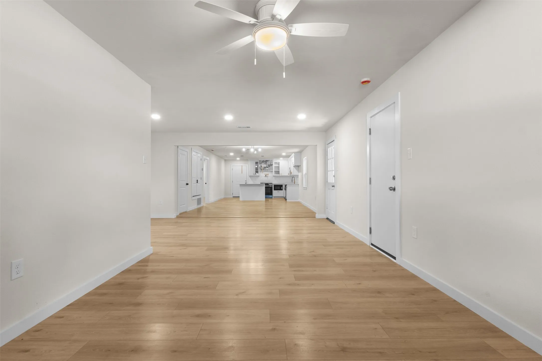 Expansive room featuring light wood-finish flooring, recessed lighting, a ceiling fan, and white walls