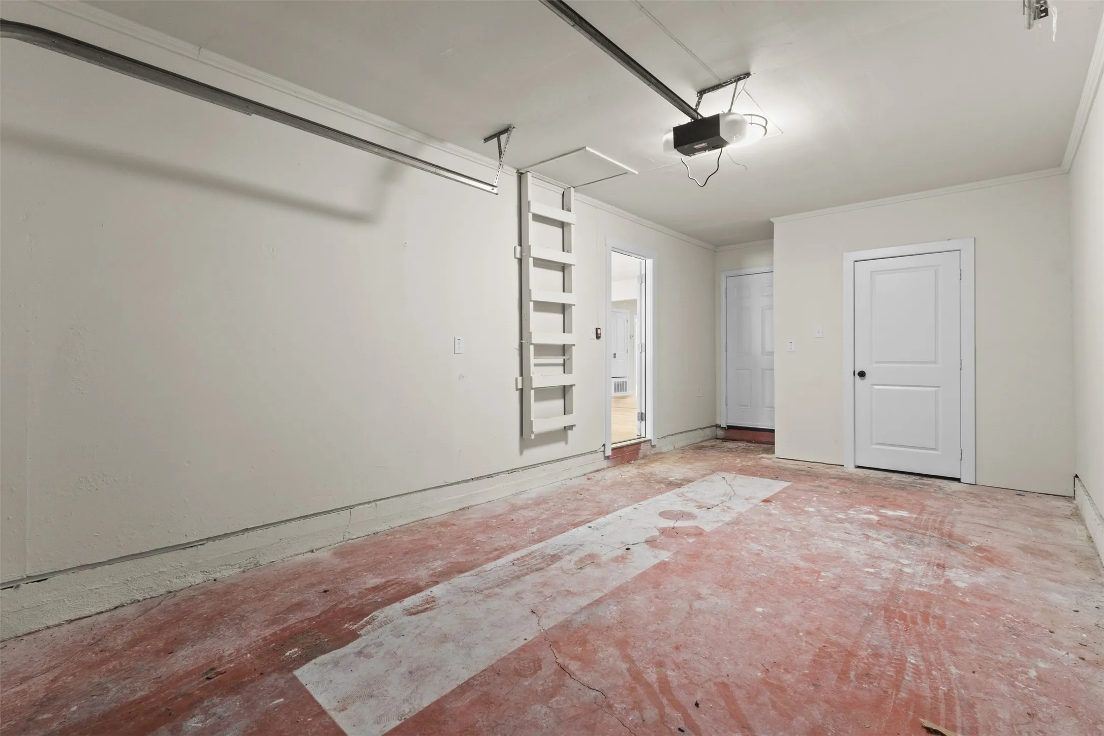 Spacious garage featuring a concrete floor, painted walls, and an attic access ladder