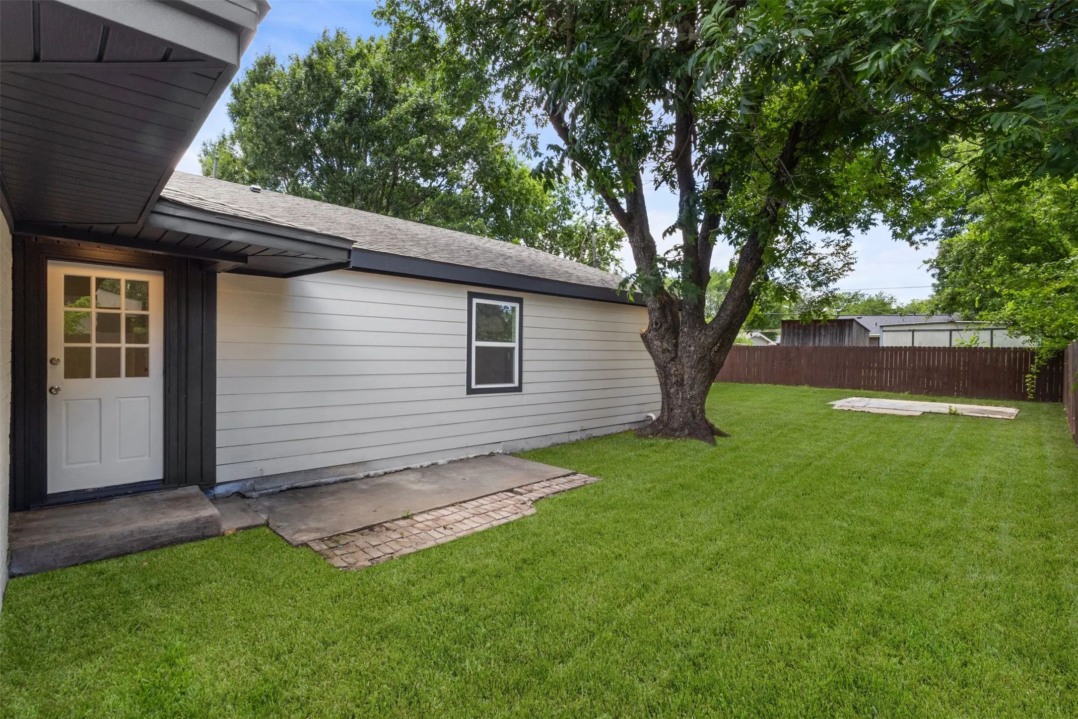 Private fenced yard featuring a mature shade tree and a concrete patio