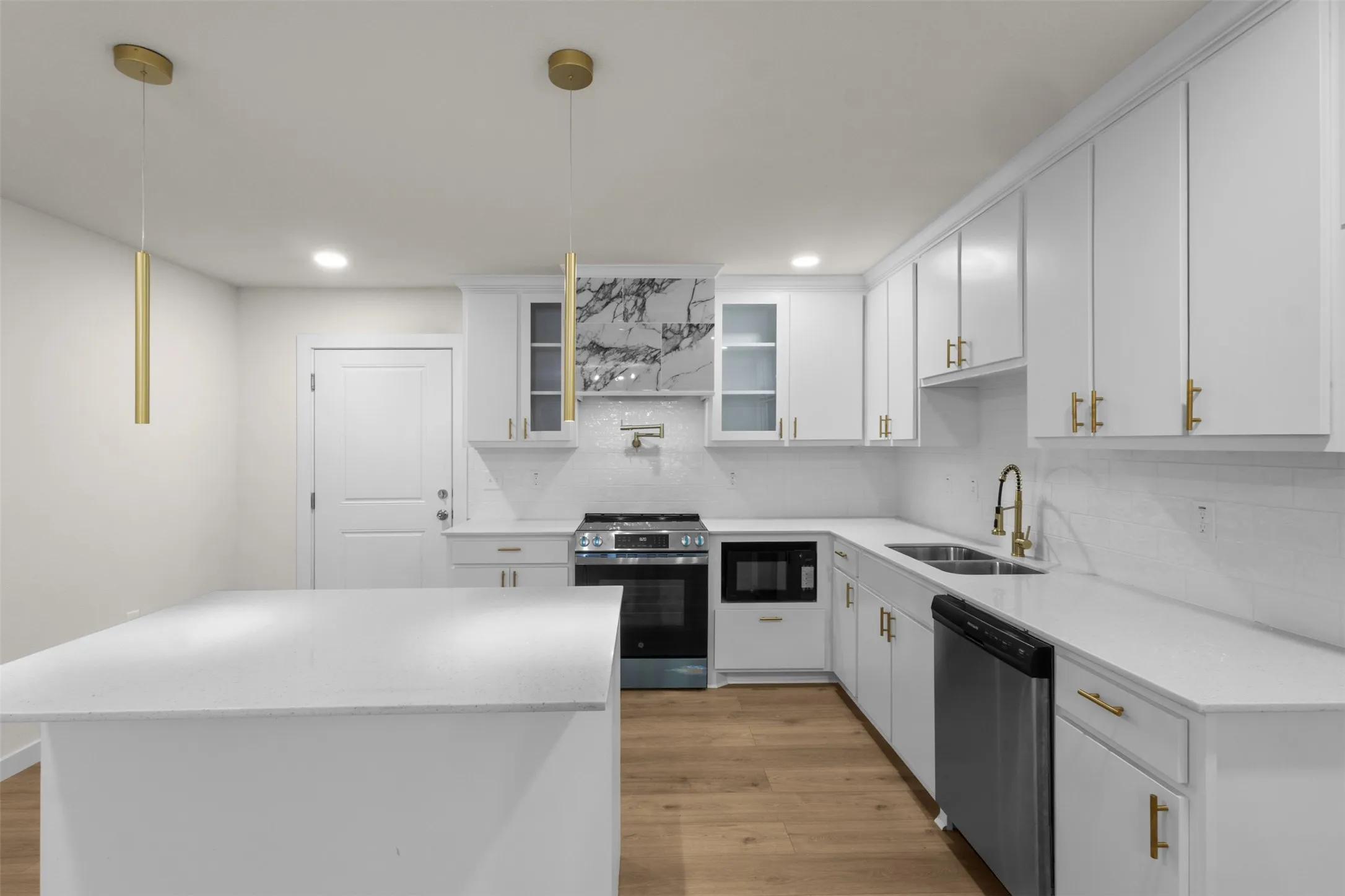 Bright kitchen featuring white cabinetry, light countertops, wood-finish flooring, stainless steel appliances, and gold-finish hardware