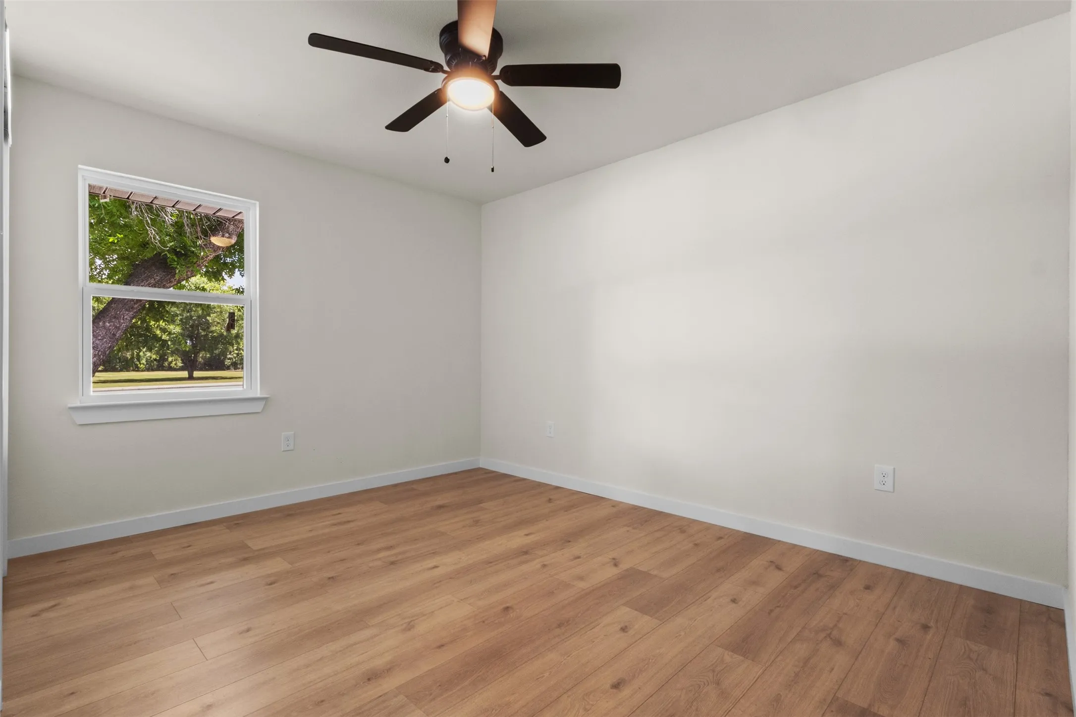 Spacious room featuring wood-finish flooring, light-toned walls, and a ceiling fan with integrated lighting