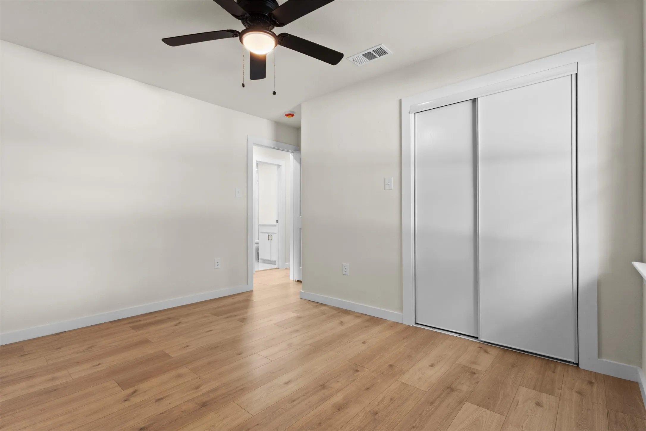 Room featuring wood-finish flooring, a ceiling fan with integrated lighting, and a sliding door closet