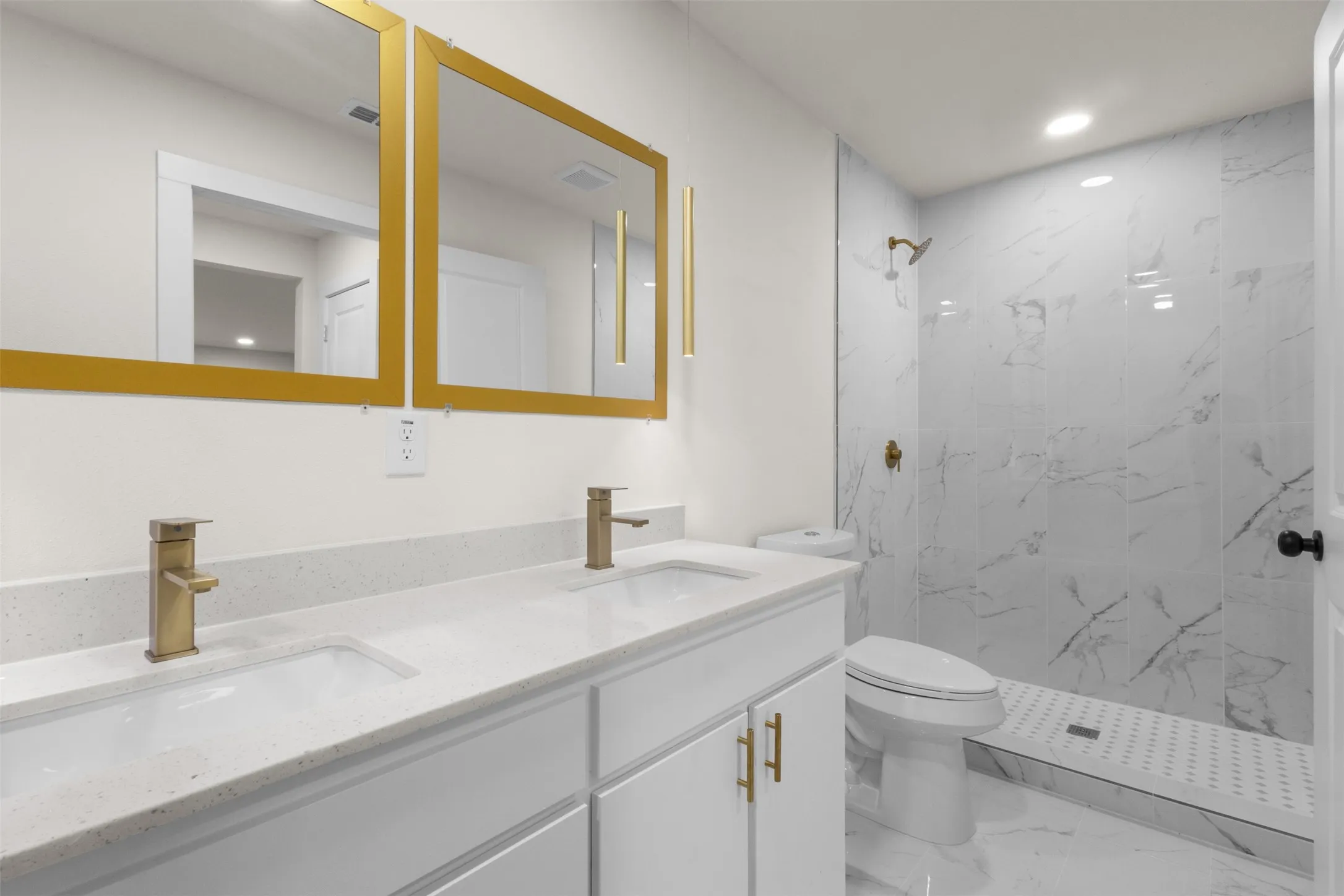 Dual vanity with white cabinetry, light-toned countertops, and brushed gold fixtures