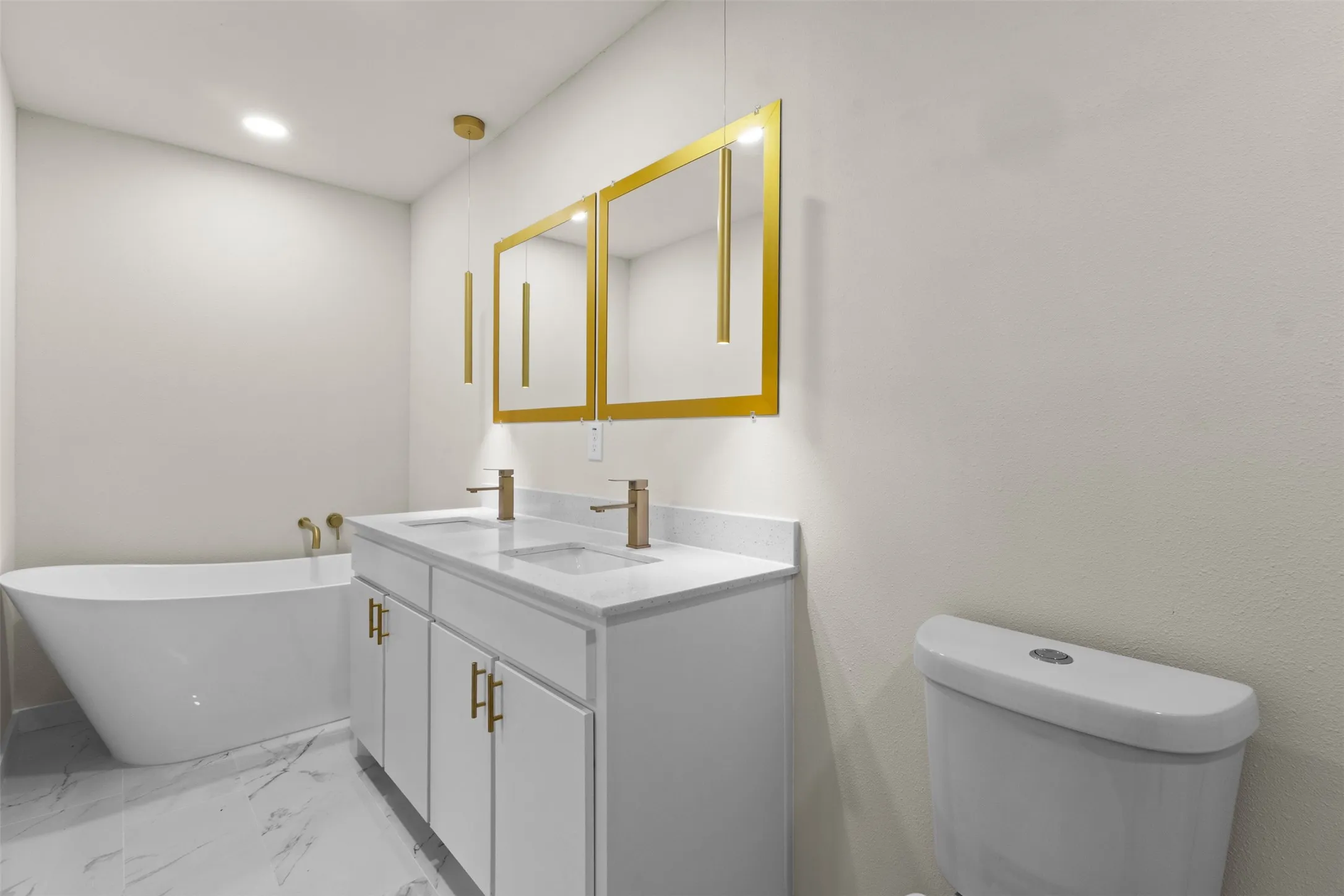 Contemporary bathroom featuring a freestanding tub, double vanity with white cabinetry, gold-toned hardware, and marble-look flooring