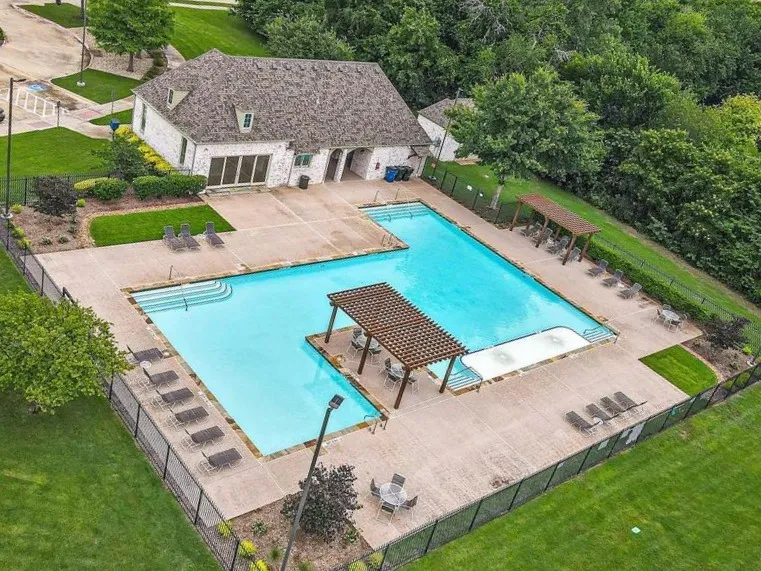 Resort-style swimming pool and spa featuring crystal-blue water, integrated sun shelf with built-in lounging area, surrounding concrete decking, and mature landscaping