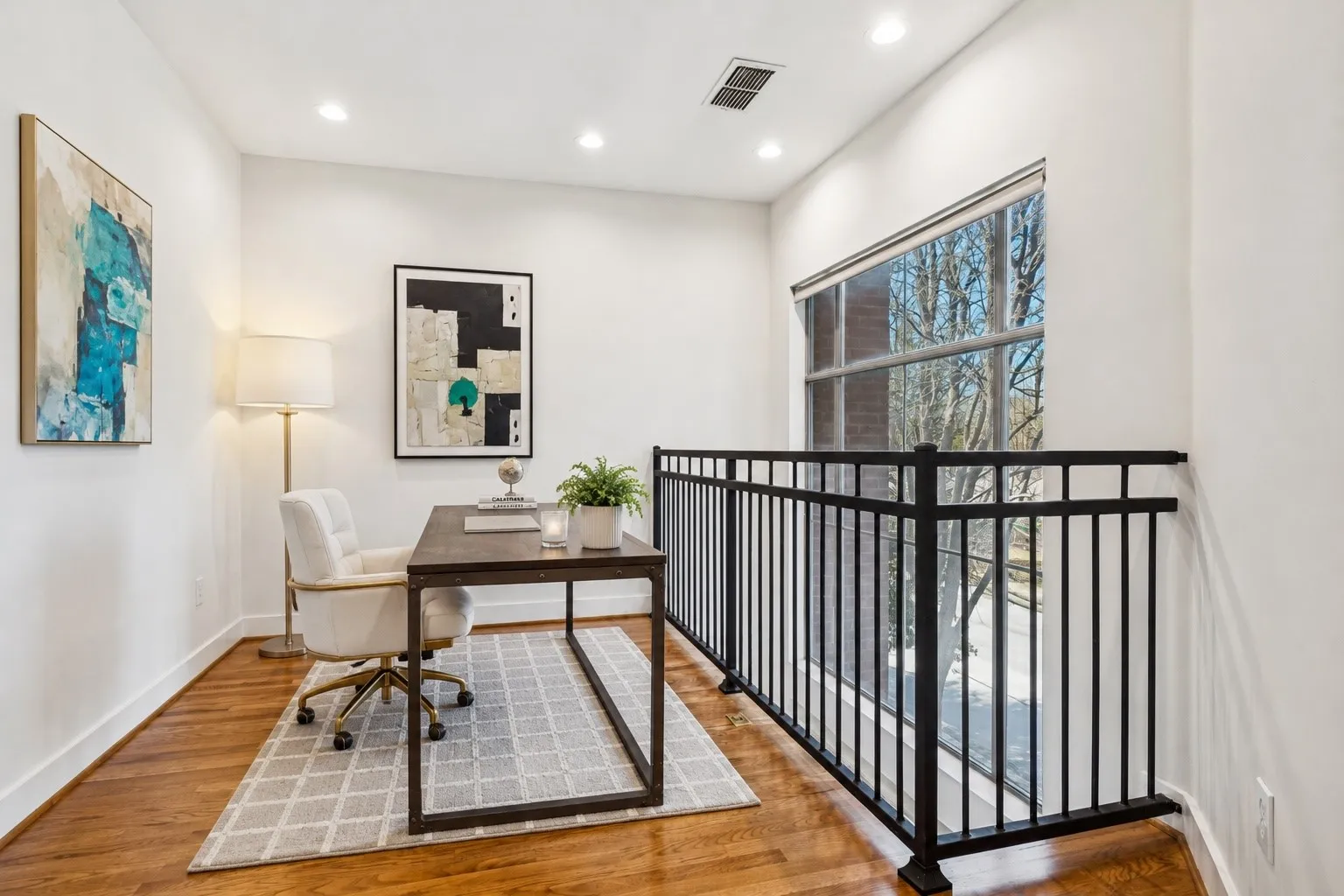 Office area featuring hardwood flooring, recessed lighting, a large picture window, a black metal railing, and white baseboards
