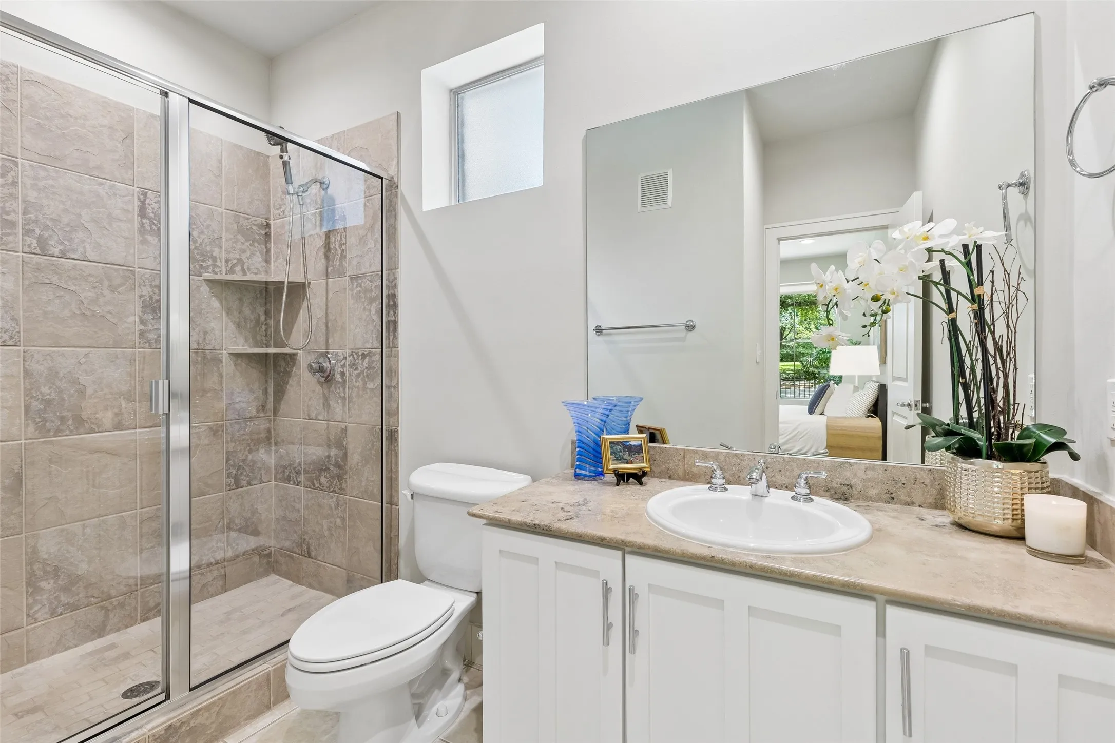 Bathroom featuring a glass-enclosed shower with tile surround, a single vanity with a light-toned countertop, a rectangular sink, and white cabinetry