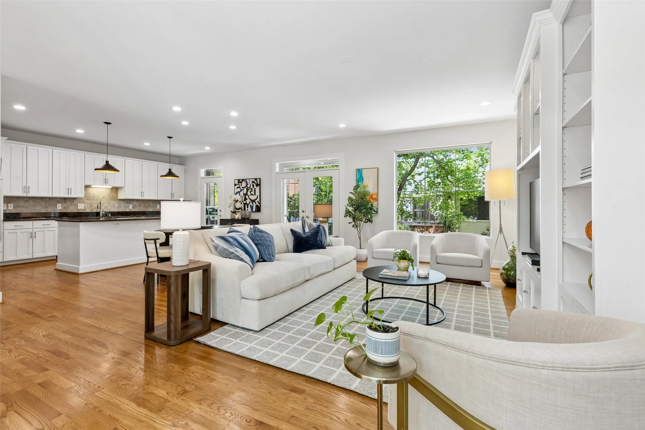 Expansive open-concept living area featuring wood-finish flooring, recessed lighting, and a kitchen with white cabinetry and dark countertops