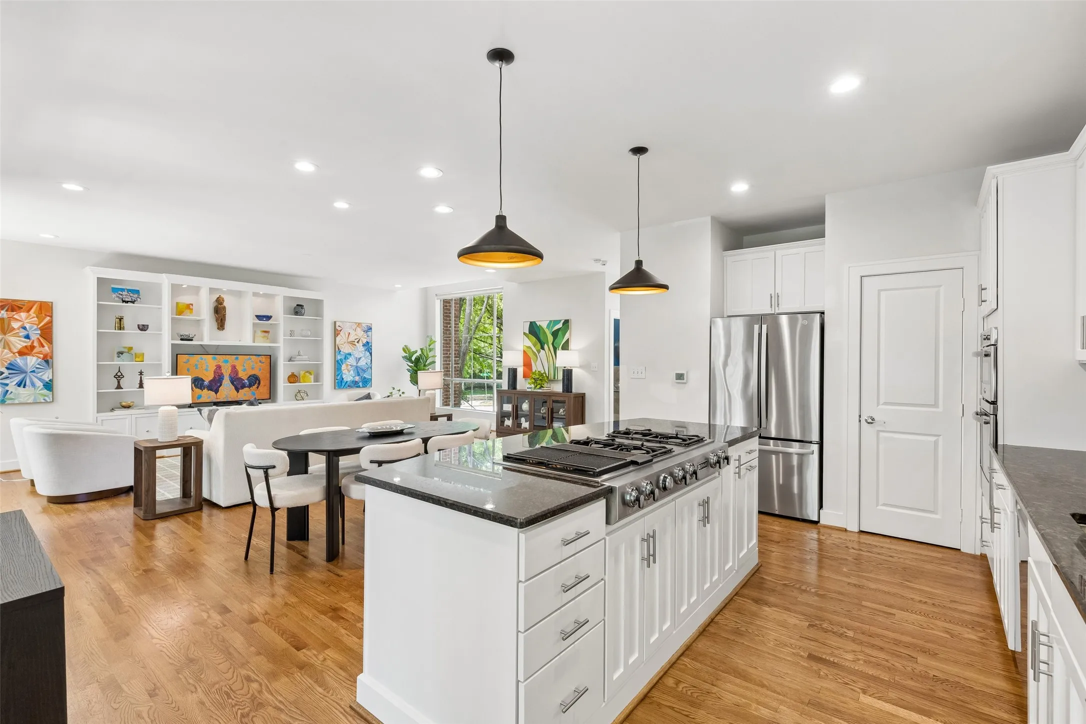 Open-concept living space featuring wood-finish flooring, a kitchen island with cooktop, a stainless steel refrigerator, built-in shelving, and recessed lighting