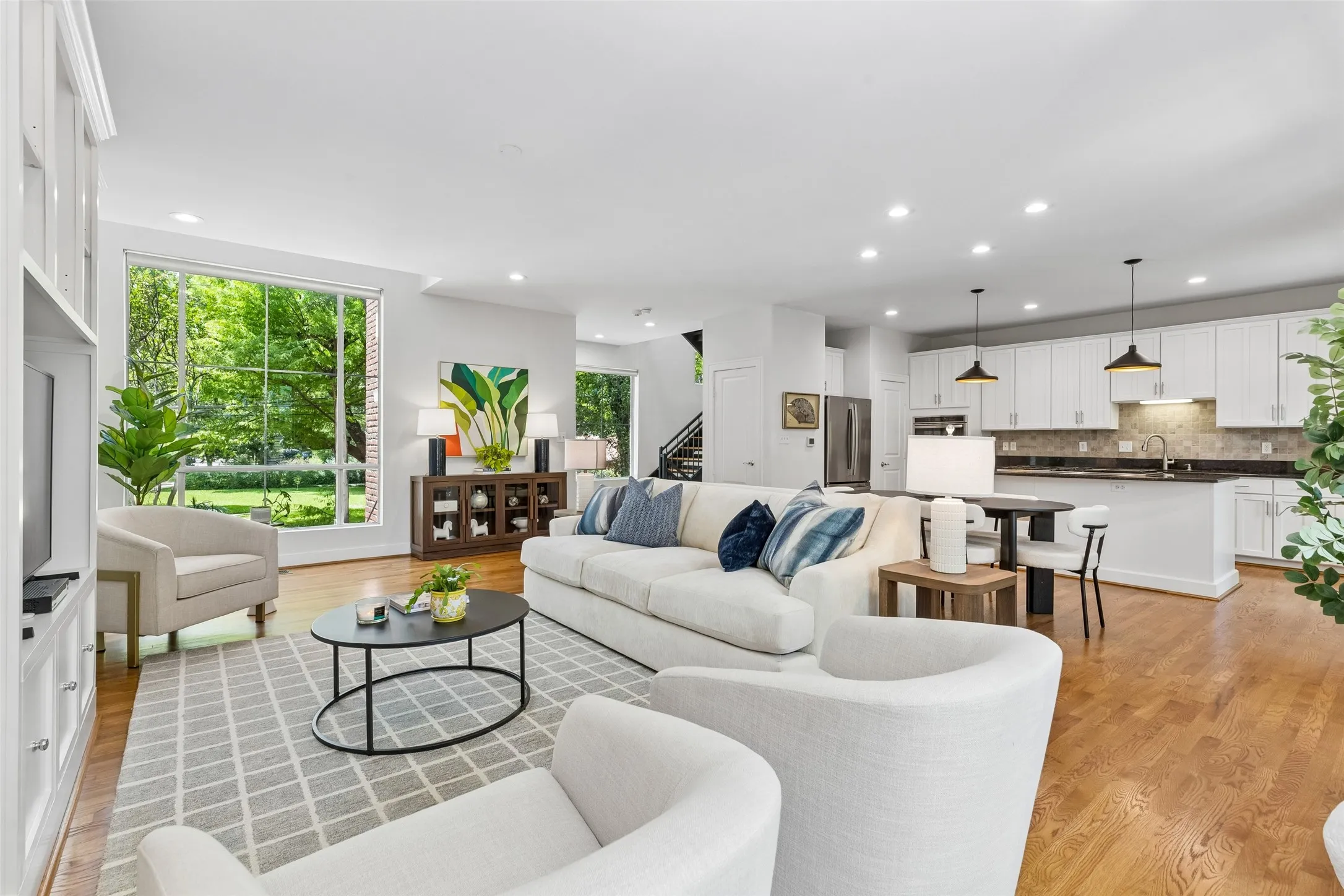 Open-concept living area with wood-finish flooring, recessed lighting, and a large picture window