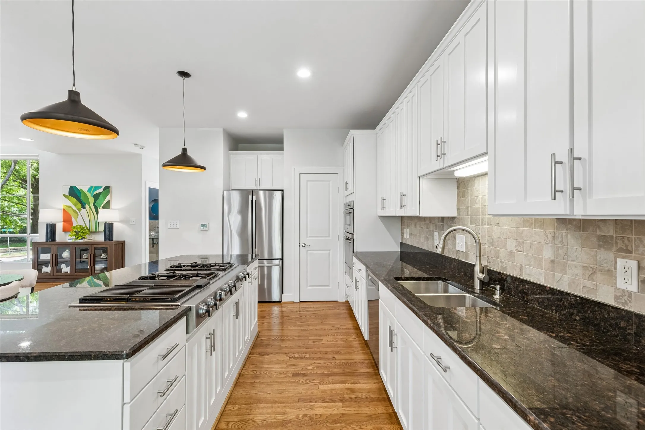 Modern kitchen featuring a large island with a gas cooktop, white cabinetry, dark stone countertops, stainless steel appliances, and wood-finish flooring