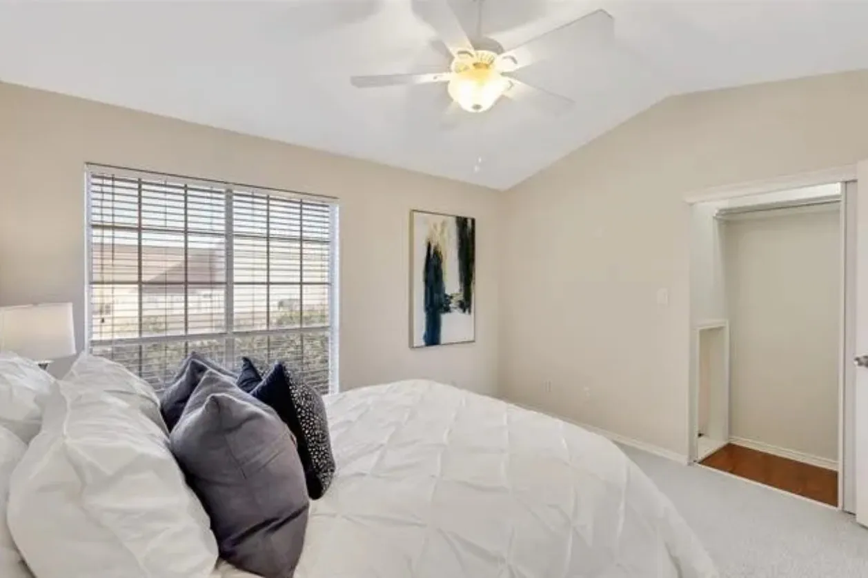 Room featuring a vaulted ceiling with a ceiling fan, a large window with blinds, and a built-in closet with wood-finish flooring