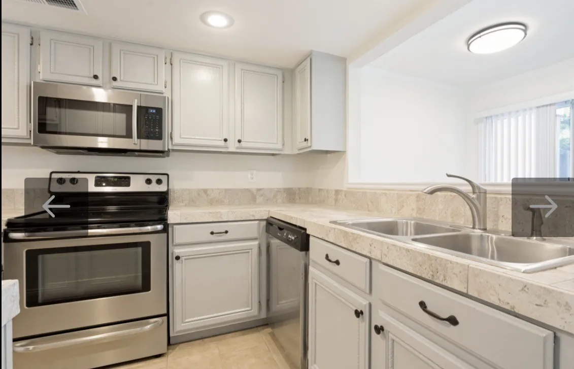 Kitchen featuring light-colored cabinetry with dark hardware, stainless steel appliances, a dual basin sink with a chrome faucet, and patterned countertops with a matching backsplash