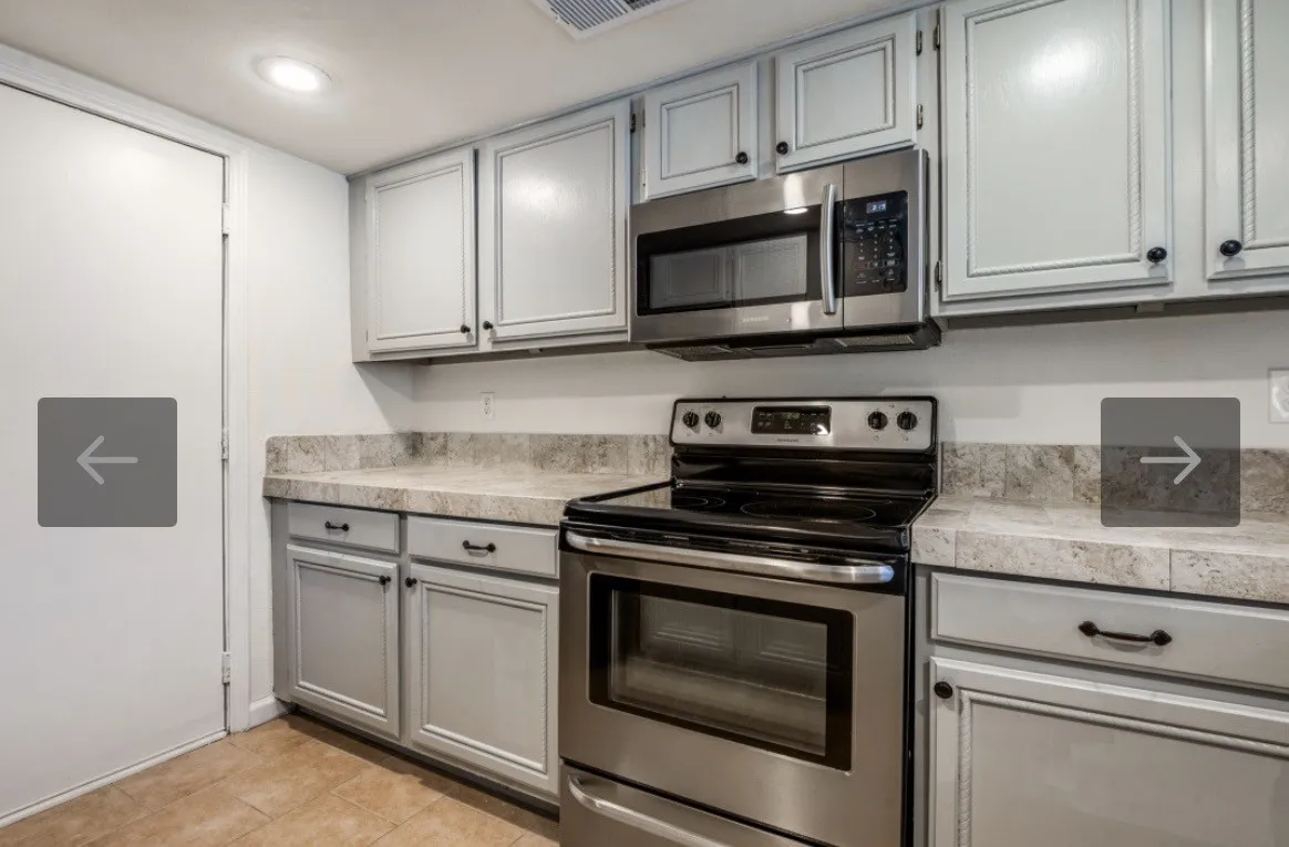 Kitchen featuring light gray cabinetry with dark hardware, stone-finish countertops with a matching backsplash, a stainless steel over-the-range microwave, and a stainless steel electric range