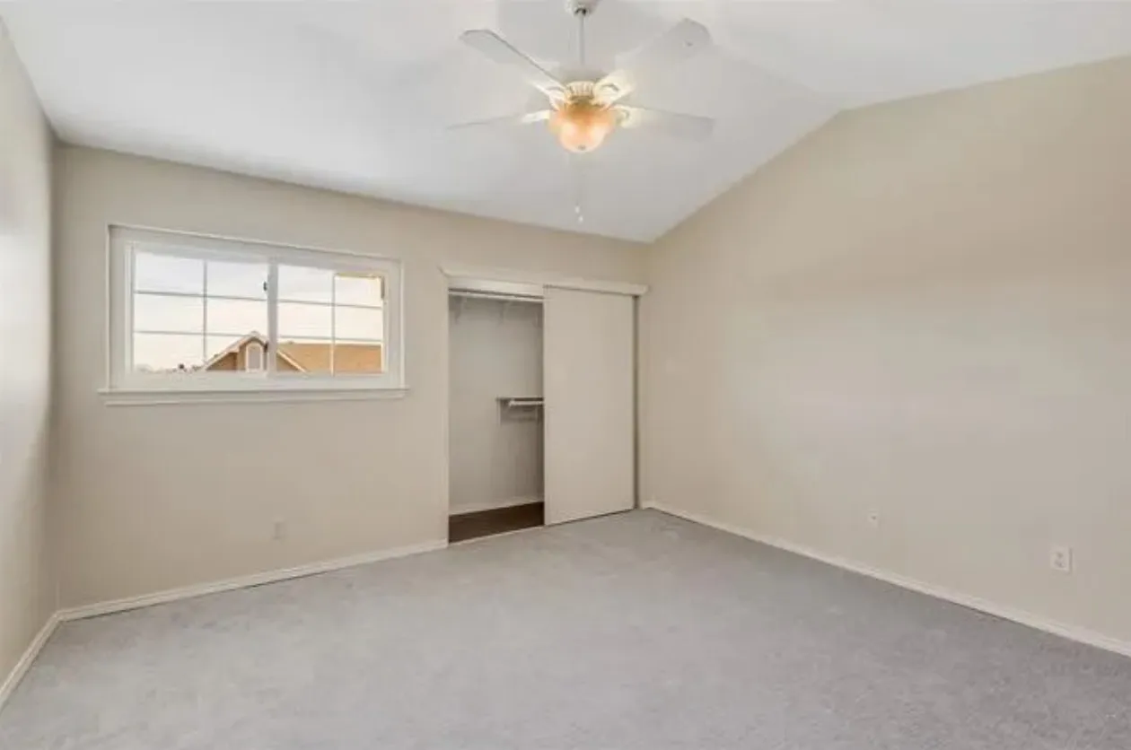 Vaulted ceiling bedroom featuring light gray carpeting, a built-in closet with sliding doors, a white ceiling fan with integrated lighting, and a white-framed window
