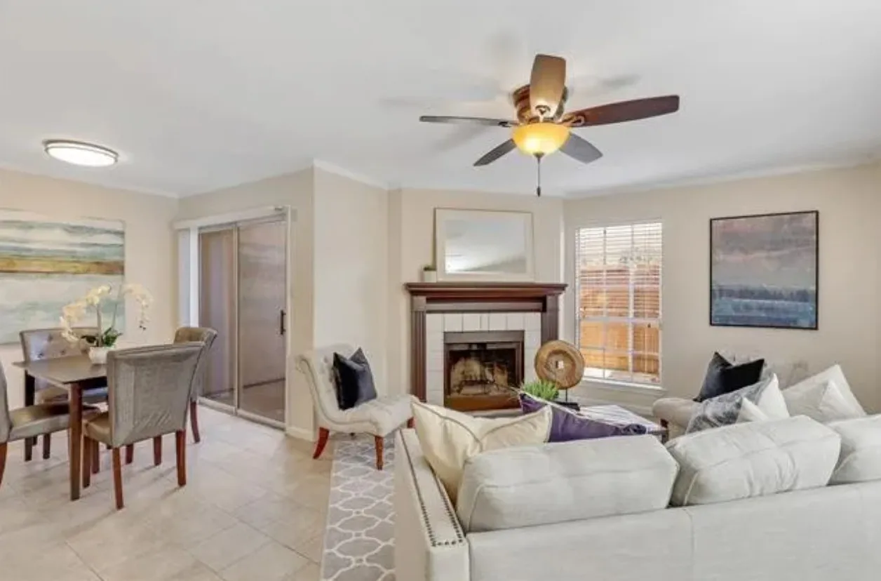 Living room featuring a wood-mantled fireplace with tile surround, ceiling fan with integrated lighting, and neutral wall tones
