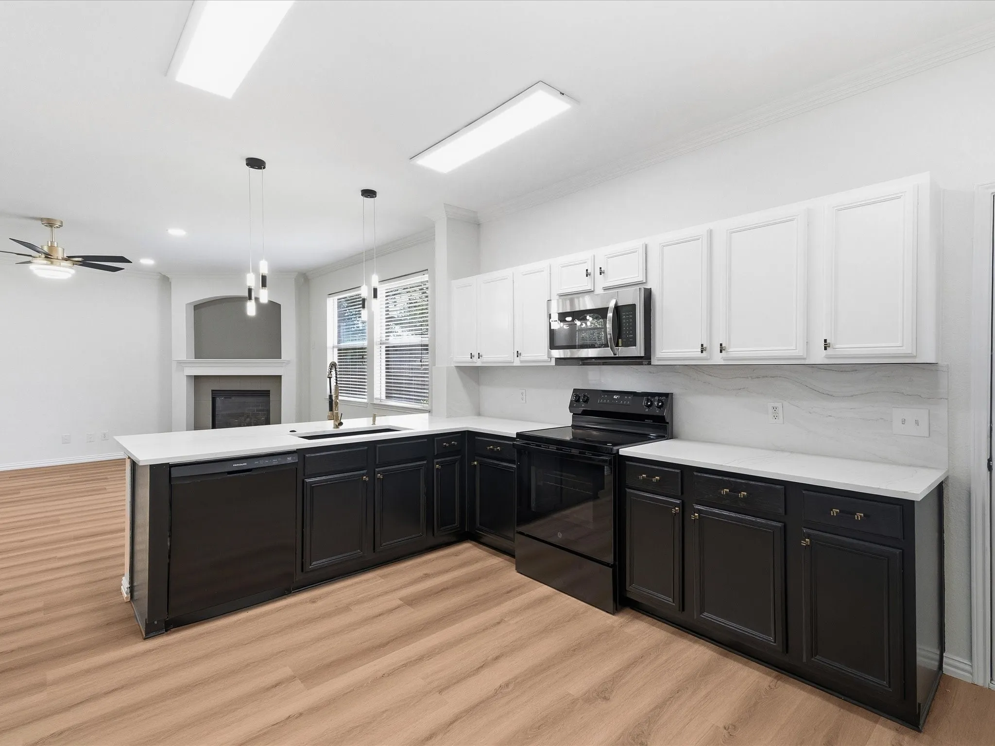 Open-concept kitchen with wood-finish flooring, featuring two-tone cabinetry, stainless steel microwave, black range, and white countertops