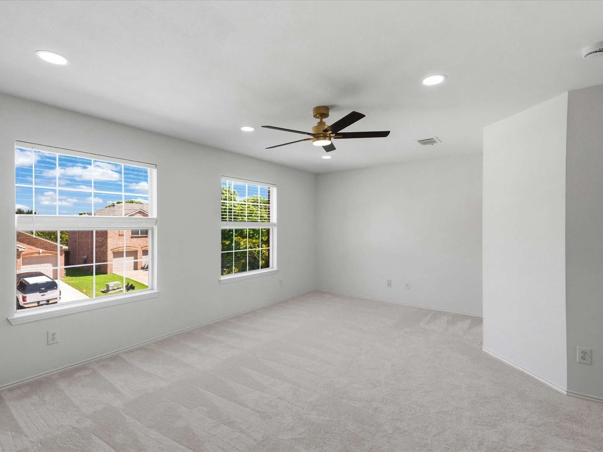 Spacious room featuring light gray carpeting, neutral wall finishes, and a contemporary ceiling fan with integrated lighting