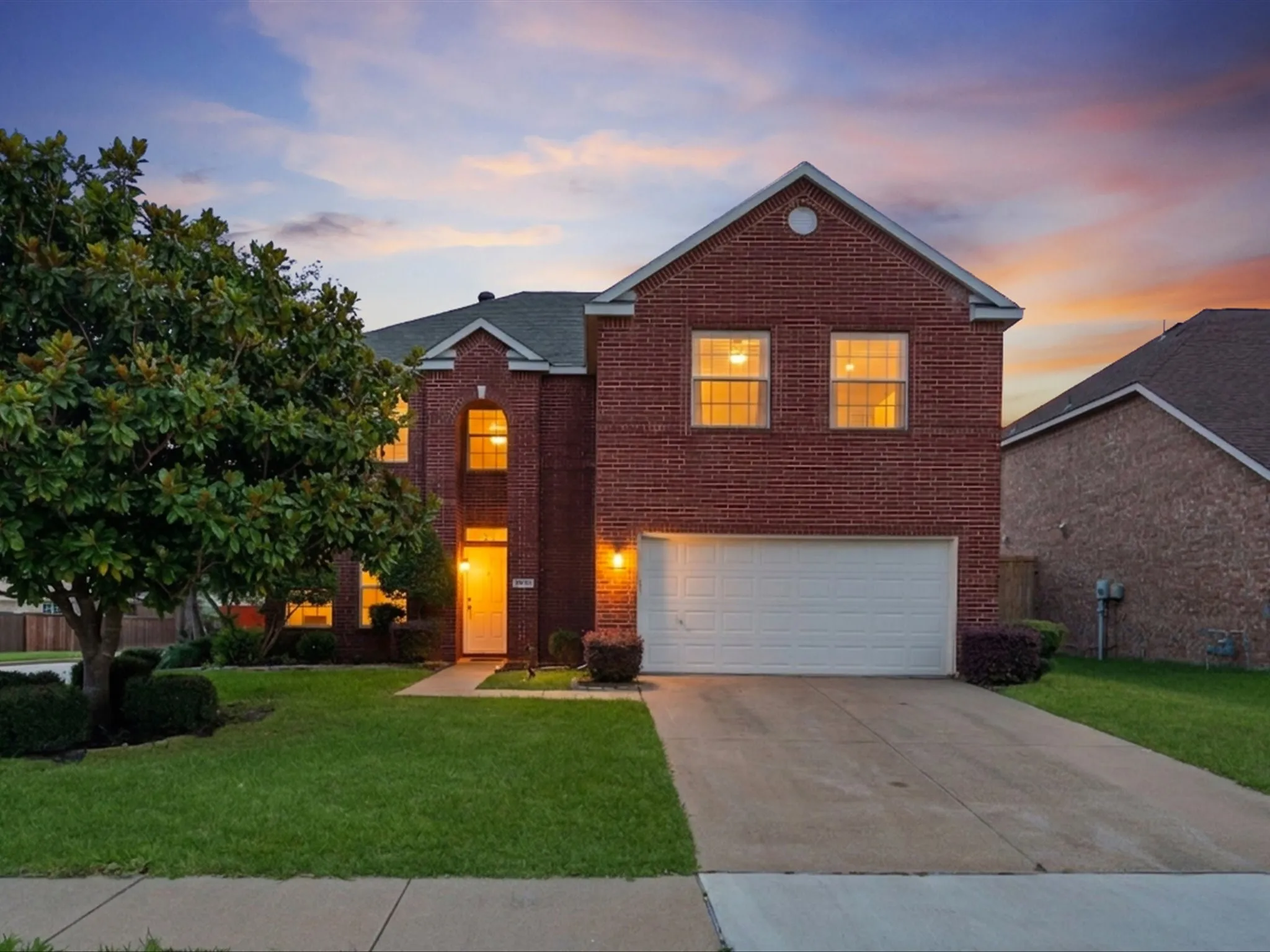 Brick facade residence featuring a two-car garage, concrete driveway, and mature landscaping