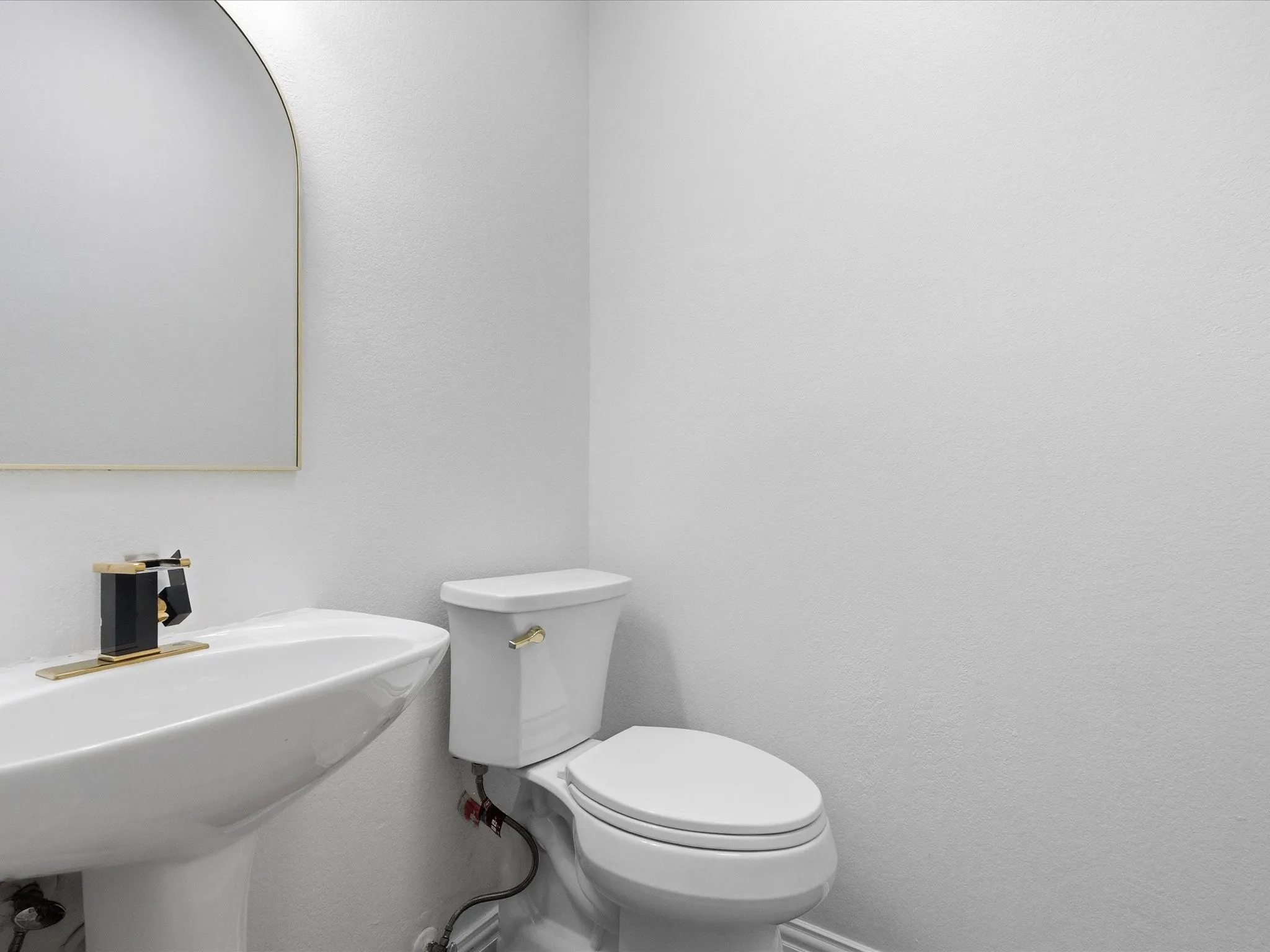 Pedestal sink with a black and gold-tone faucet, arched mirror, and white toilet
