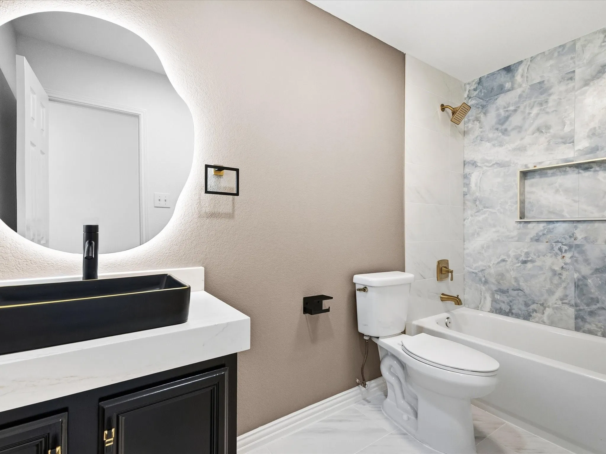 Bathroom featuring a freestanding tub with brass fixtures, a built-in shower niche, and variegated blue and white wall tile
