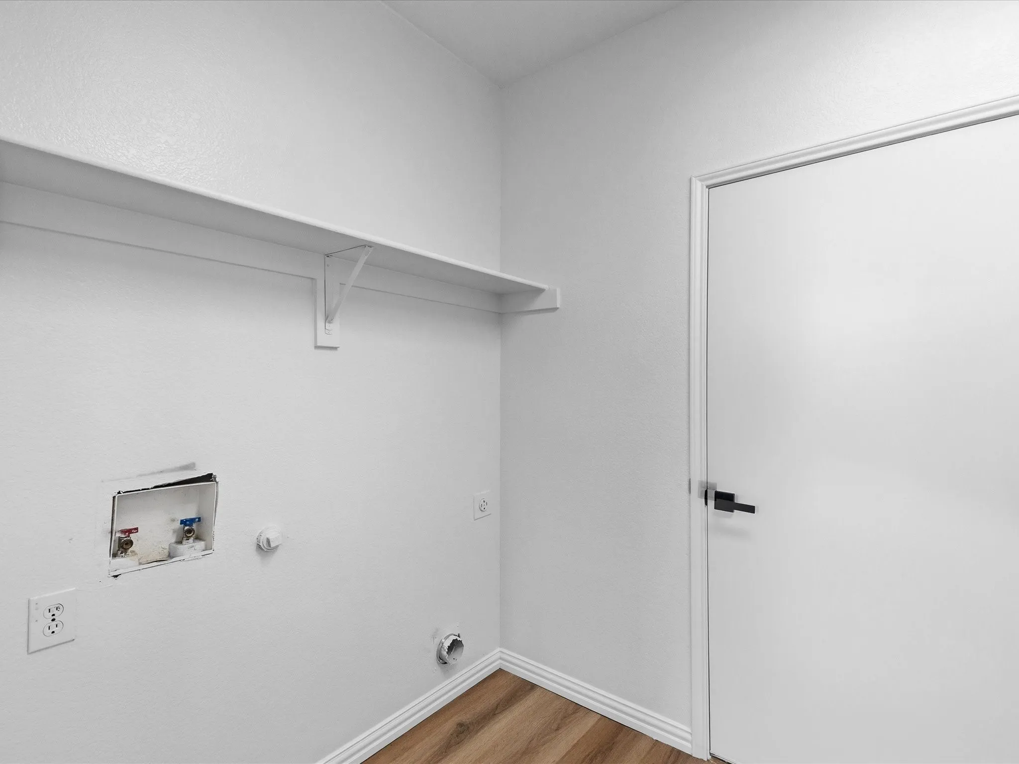 Laundry area featuring wood-finish flooring, white walls, and a built-in shelf