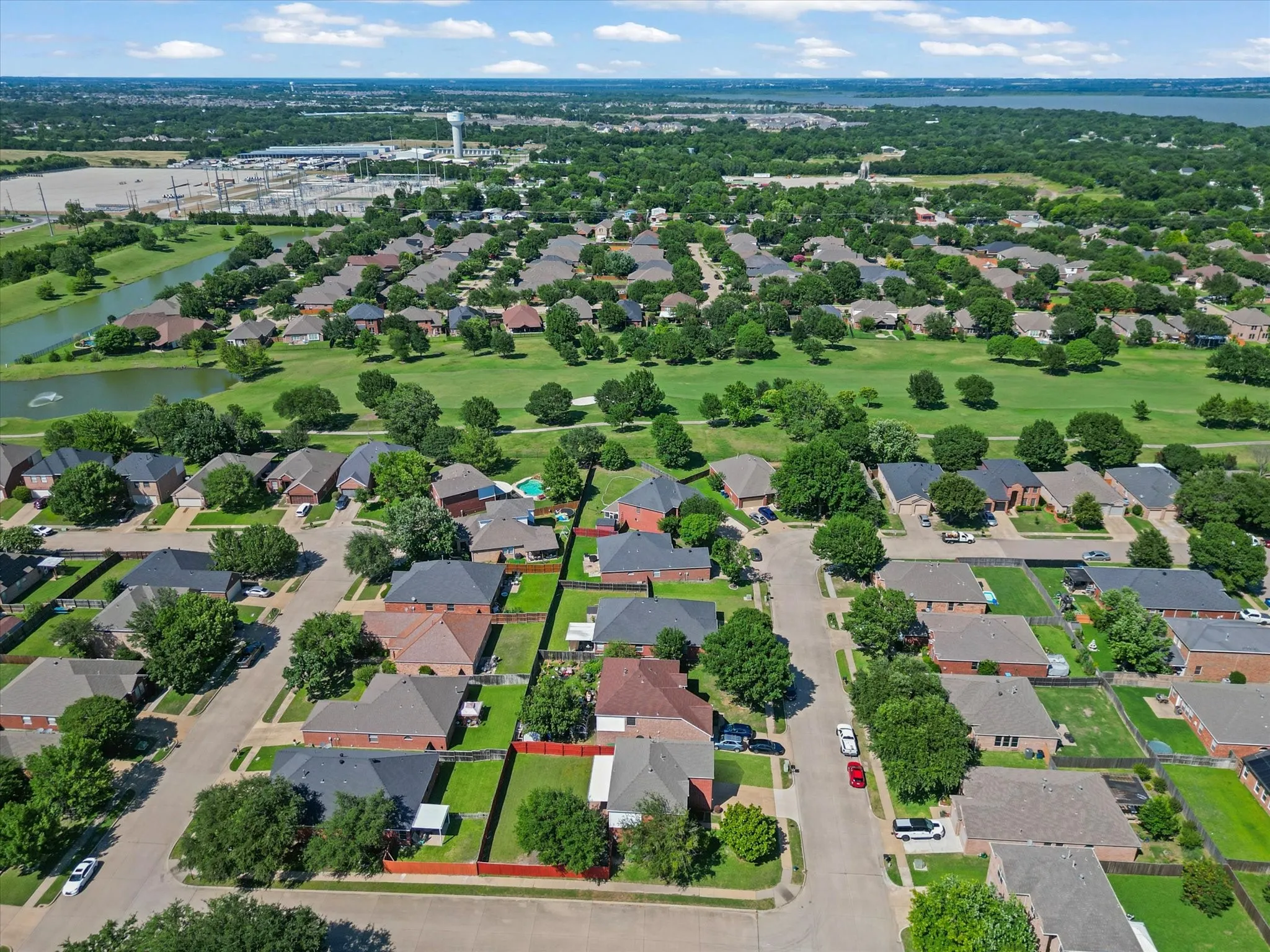 Residential neighborhood featuring mature trees, paved streets, and a large green space