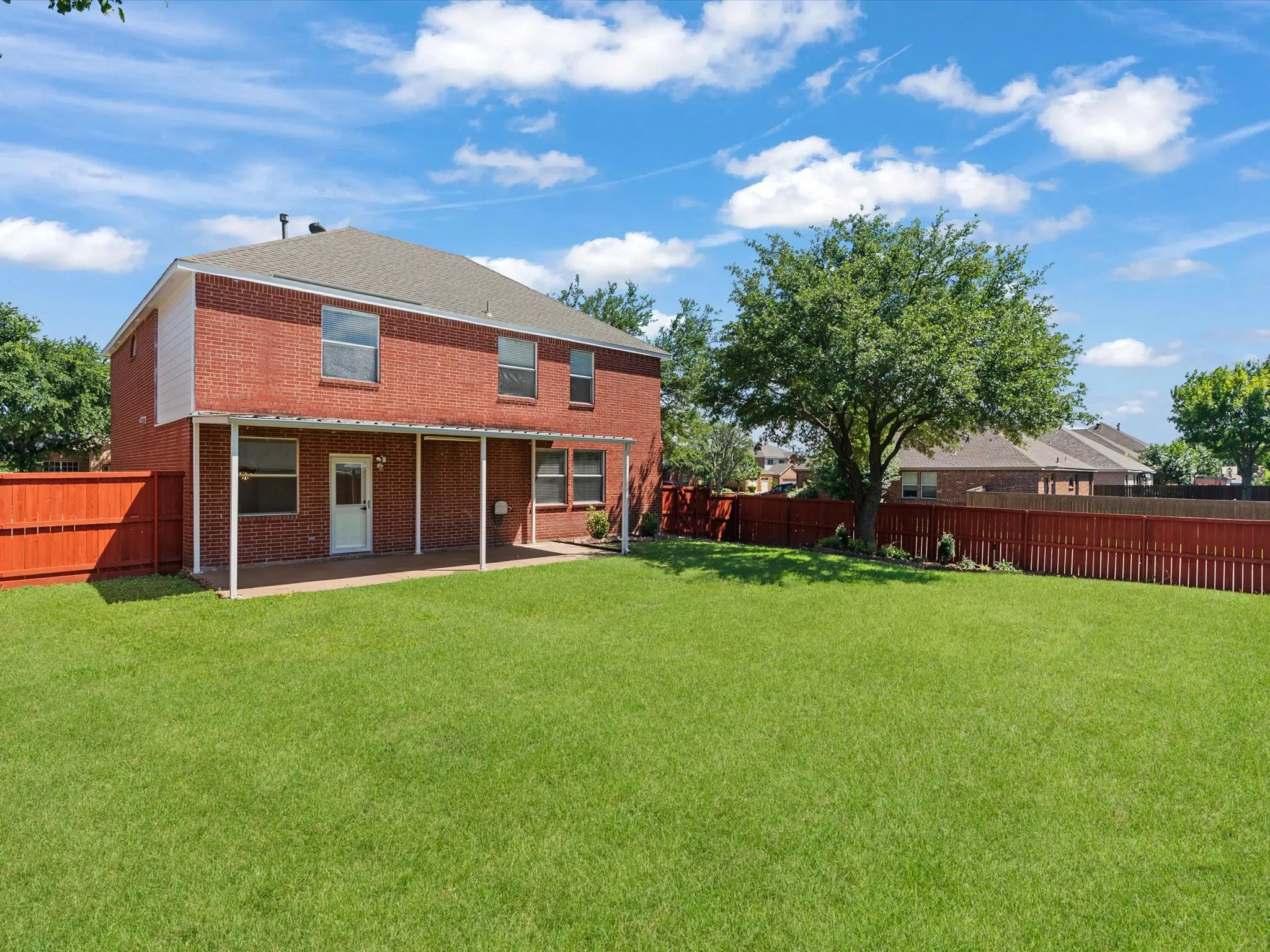 Expansive green lawn with a red brick exterior and a covered patio
