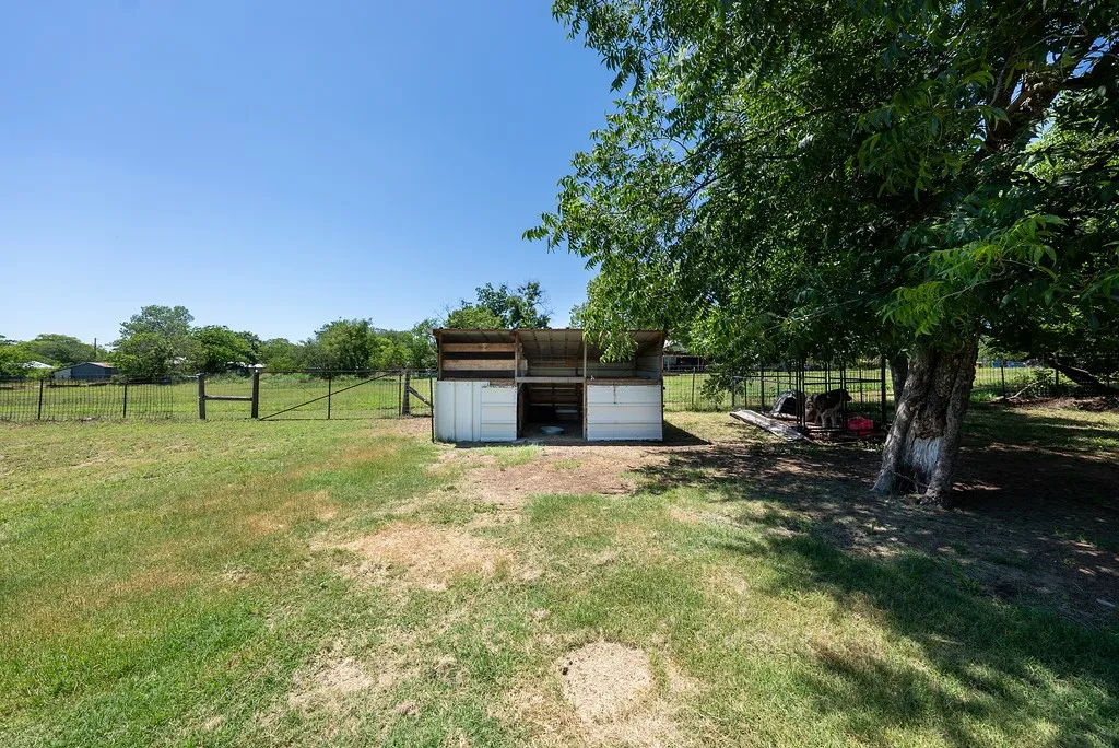Grassy outdoor area featuring a wood fence, gate, and mature trees