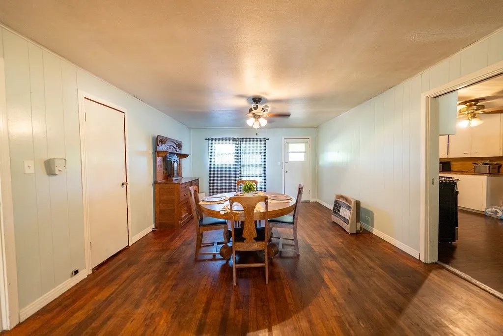 Spacious interior with wood-finish flooring, light-colored vertical paneling, and an overhead ceiling fan with lighting