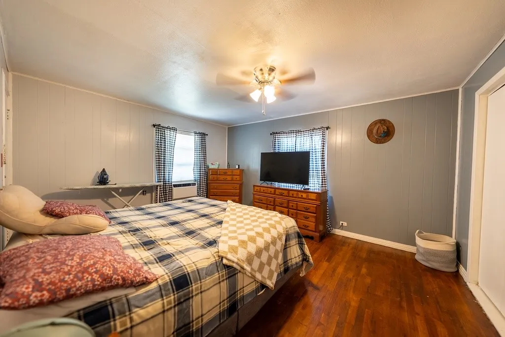 Spacious room featuring wood-finish flooring, two windows with checked curtains, and a ceiling fan light fixture