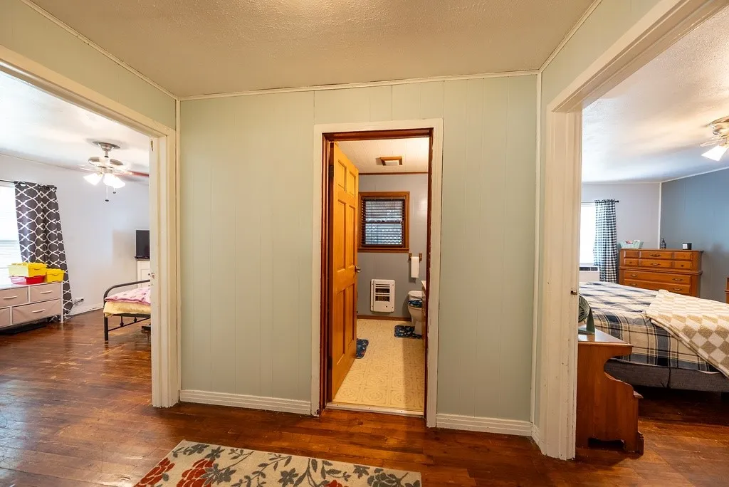 Hallway featuring wood-finish flooring, light blue paneled walls, and three doorways with white trim