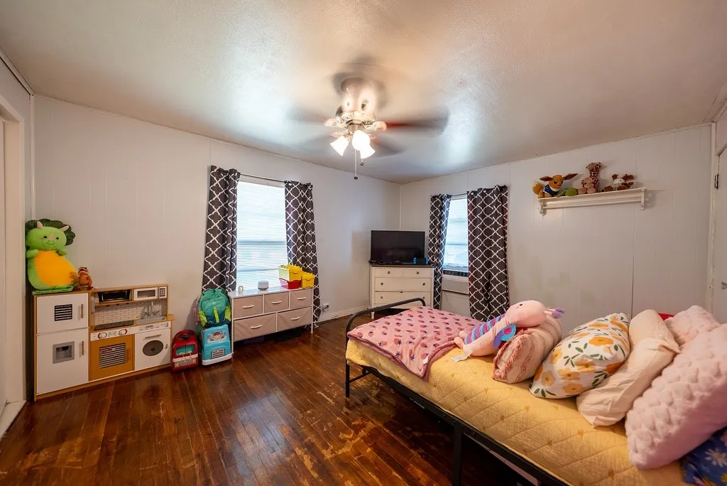 Room featuring wood-finish flooring, white paneled walls, and two windows with dark patterned curtains