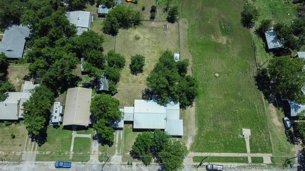 Expansive lot featuring a large grassy area, mature trees, and a gravel driveway