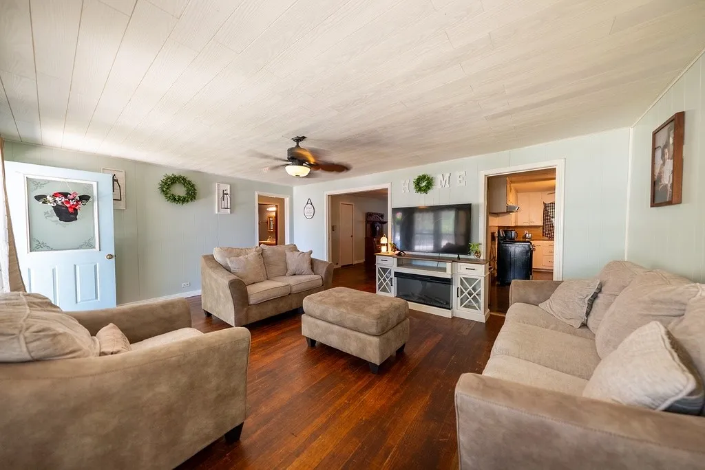 Spacious living area featuring wood-finish flooring, a ceiling fan with integrated lighting, and light blue wall tones