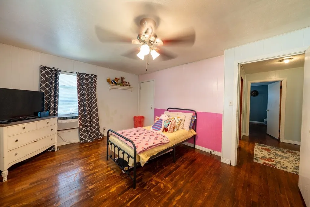 Interior room featuring wood-finish flooring, a ceiling fan with integrated lighting, and a window with patterned drapes