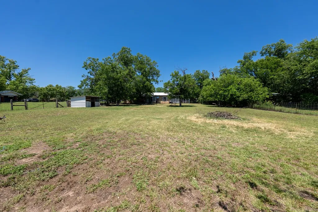Expansive parcel featuring a large grassy area, mature trees, a small outbuilding, and partial fencing