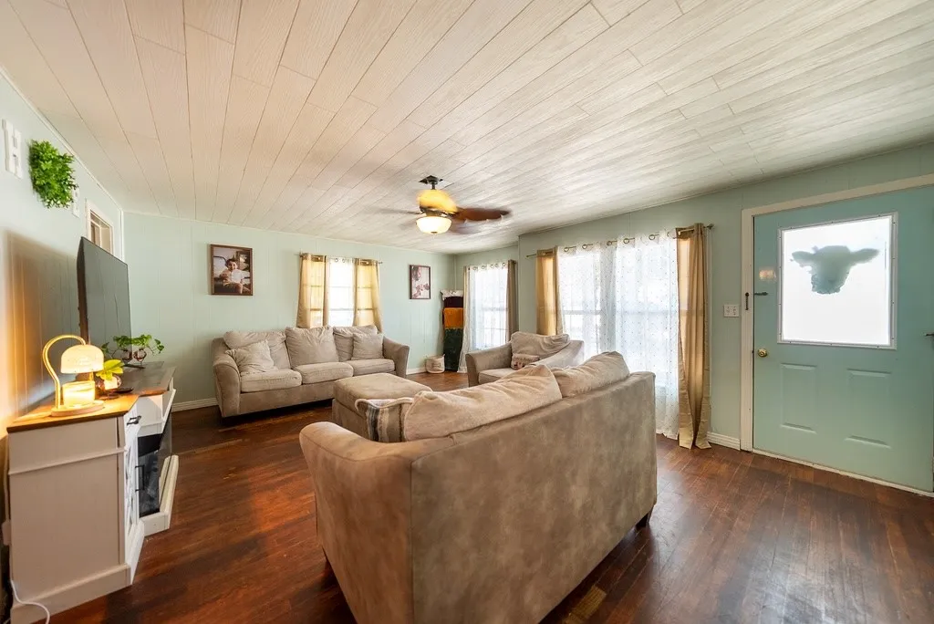 Living area featuring wood-finish flooring, a light-colored wood plank ceiling, and a ceiling fan with integrated lighting