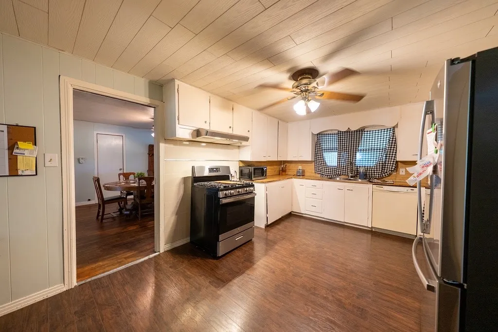 Kitchen featuring wood-finish flooring, white cabinetry, a stainless steel refrigerator, and a gas range