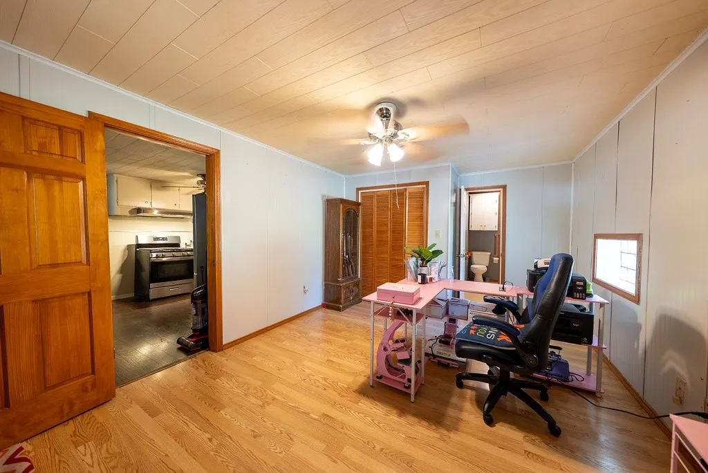 Bright room featuring wood-finish flooring, a ceiling fan with integrated lighting, and a paneled ceiling.  Could be considered the primary bedroom because it has a full bath en suite.