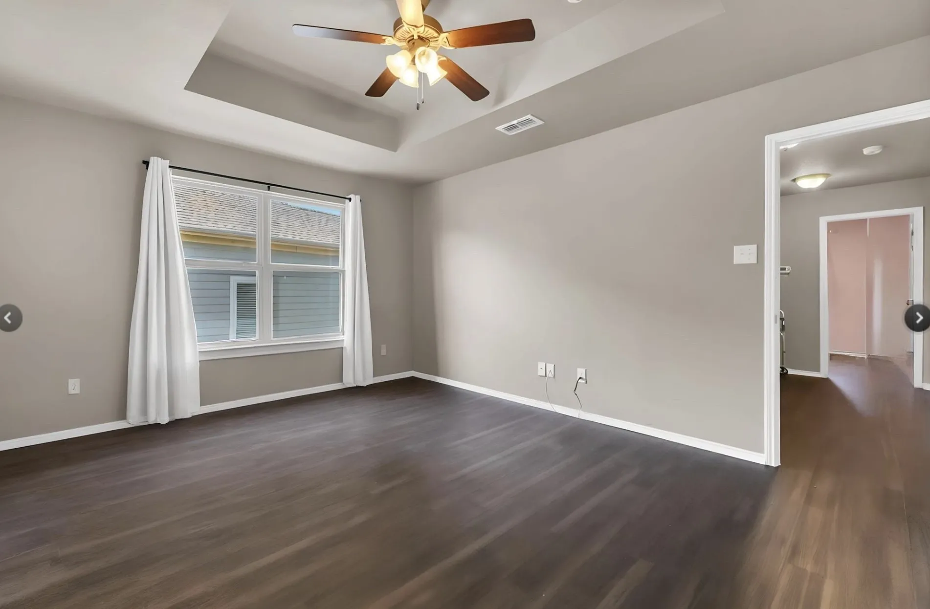 Spacious room featuring wood-finish flooring, a tray ceiling, and a ceiling fan
