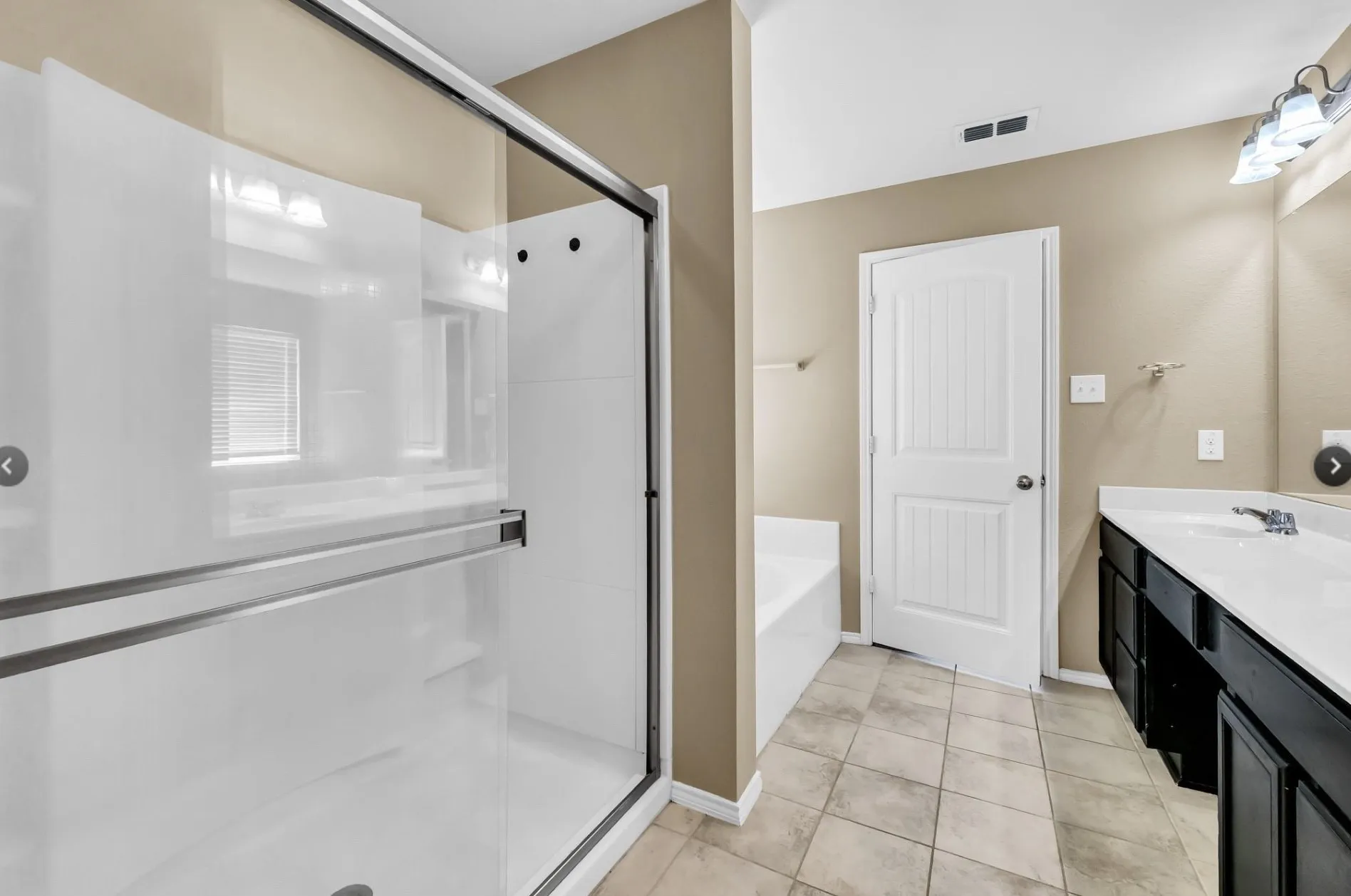 Glass-enclosed shower with white surround, featuring a white built-in tub, a dark wood-finish vanity with dual sinks, and tiled flooring