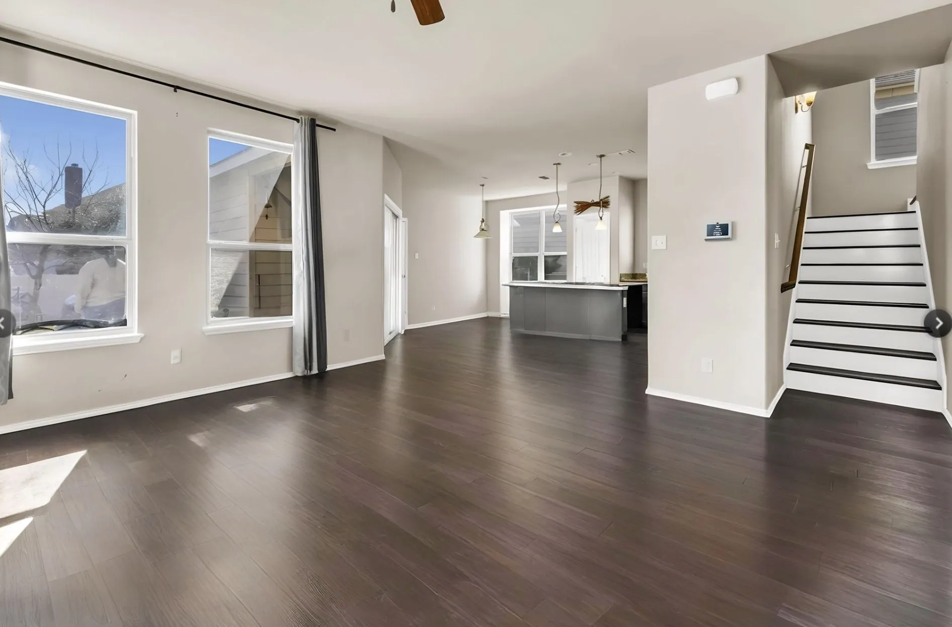 Expansive living area featuring rich wood-finish flooring, abundant natural light from multiple windows, and neutral wall tones