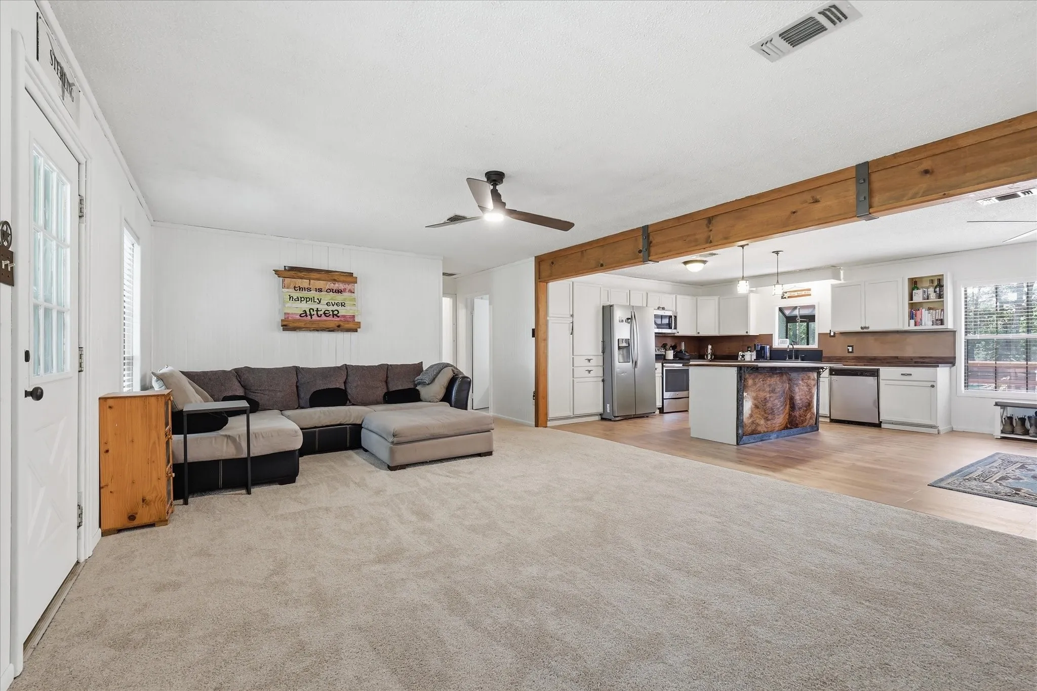 Spacious living area featuring light-toned carpeting and white paneled walls
