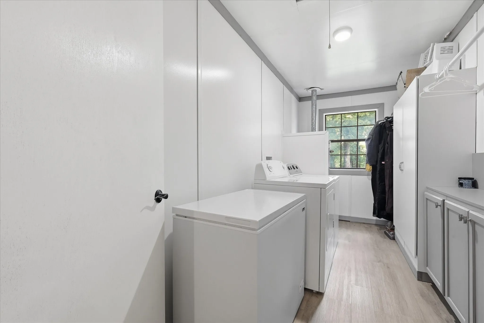 Utility room featuring wood-finish flooring, white paneled walls, and a large window with exterior foliage