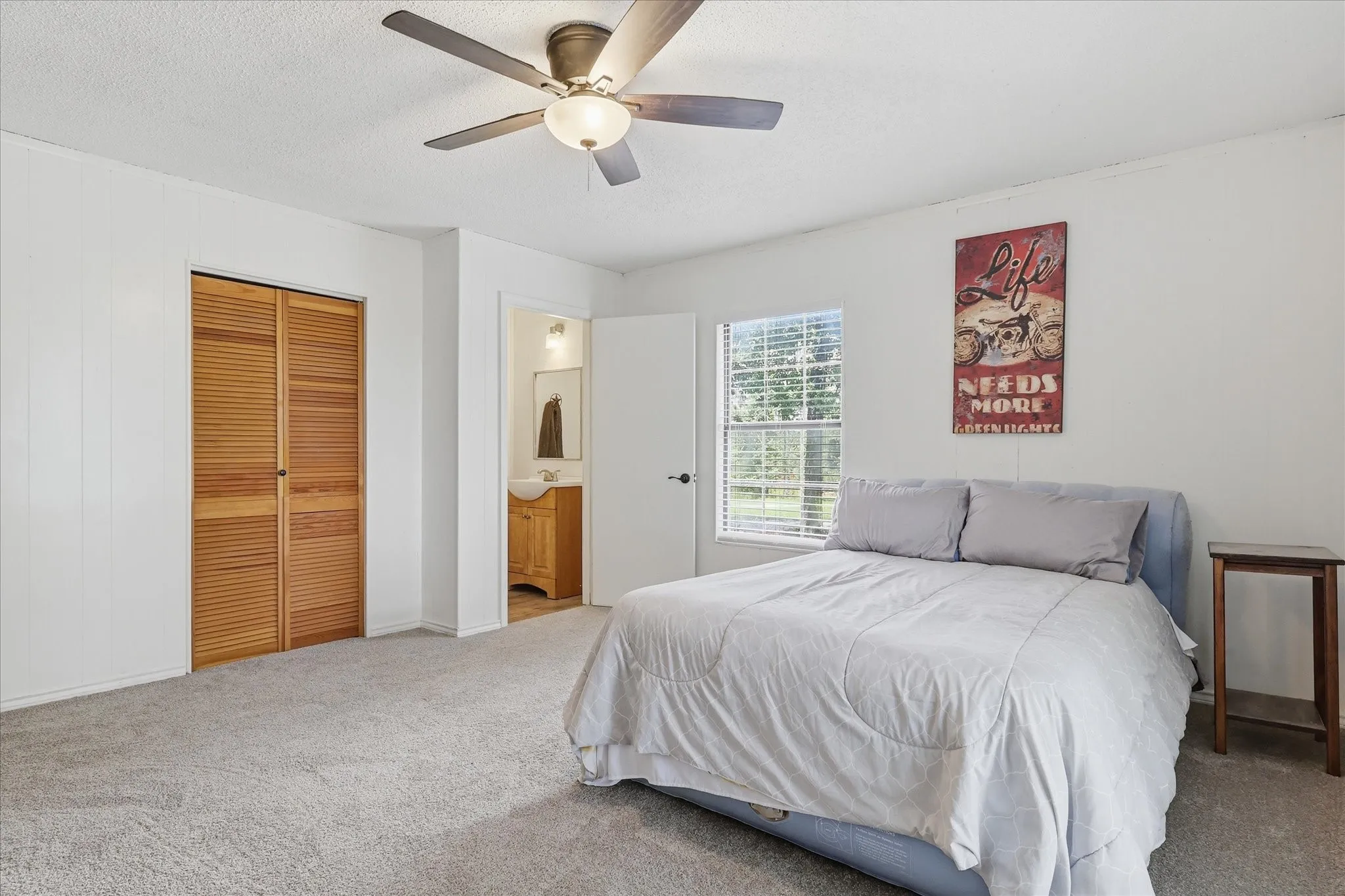Spacious room featuring light gray carpeting, a ceiling fan with integrated lighting, and a window providing natural illumination