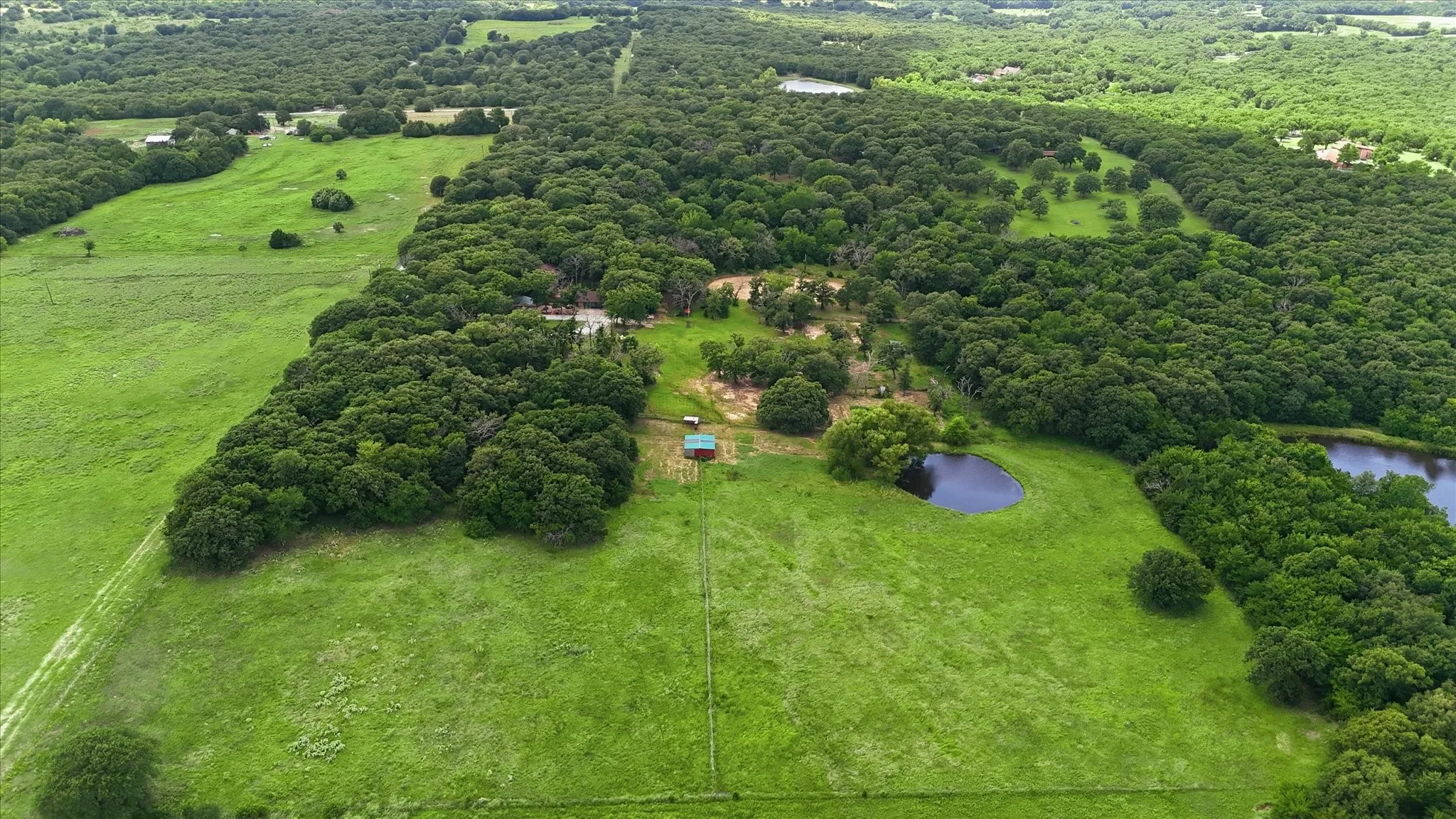 Expansive property featuring dense wooded areas, open green pastures, and two visible ponds